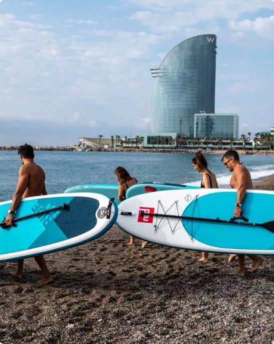 Groupe de personnes se dirigeant vers l'eau avec des planches et des rames pour faire du paddle surf sur la plage de la Barceloneta