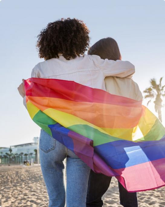 Two people hugging with the LGBT flag in the background