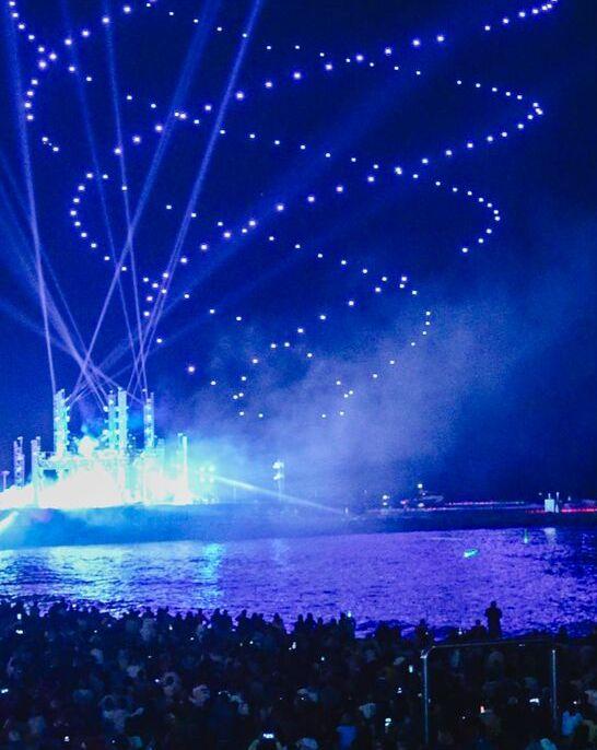 Barcelona, far al món. Gent a la platja mira un espectacle de drons.